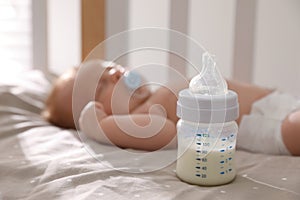 Healthy baby sleeping in cot, focus on bottle with milk