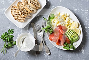 Healthy balanced breakfast or snack - smoked salmon, egg salad and avocado. On a gray background, top view. Healthy food