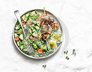 Healthy balanced lunch bowl - turkey kebab skewers, quinoa, avocado, cucumber salad and boiled egg on light background, top view