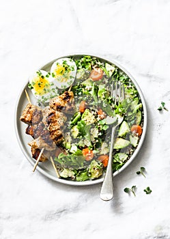 Healthy balanced lunch bowl - turkey kebab skewers, quinoa, avocado, cucumber salad and boiled egg on light background, top view