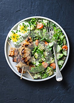 Healthy balanced lunch bowl - turkey skewers, quinoa, avocado, cucumber salad and boiled egg on dark background, top view.