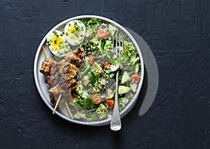 Healthy balanced lunch bowl - turkey skewers, quinoa, avocado, cucumber salad and boiled egg on dark background, top view.