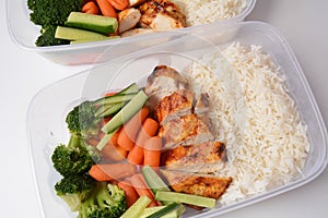 Healthy balanced lunch boxes. Grilled chicken, carrots, cucumbers, broccoli, and white rice.