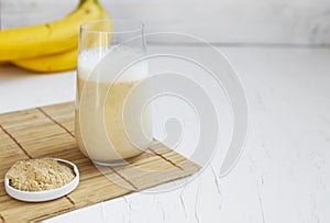 Healthy banana smoothie on wooden board with maca and protein on white background