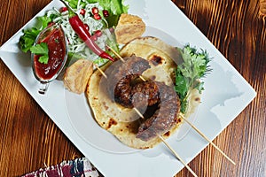 Healthy barbecued lean cubed pork kebabs served with a corn tortilla and fresh lettuce and tomato salad, close up view