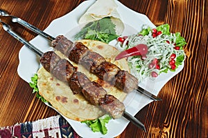 Healthy barbecued lean cubed pork kebabs served with a corn tortilla and fresh lettuce and tomato salad, close up view