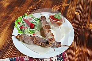 Healthy barbecued lean cubed pork kebabs served with a corn tortilla and fresh lettuce and tomato salad, close up view