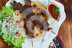 Healthy barbecued lean cubed pork kebabs served with a corn tortilla and fresh lettuce and tomato salad, close up view