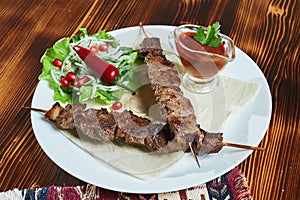 Healthy barbecued lean cubed pork kebabs served with a corn tortilla and fresh lettuce and tomato salad, close up view