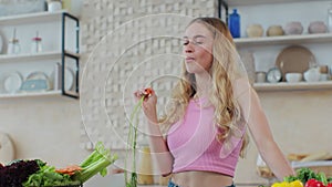 Healthy beautiful woman tasting and eating a carrot in the kitchen. Preparing fresh vegetable salad. Healthy eating and