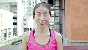 Healthy beautiful young Asian runner woman feeling happy smiling and looking to camera after running on street in urban city.