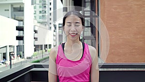 Healthy beautiful young Asian runner woman feeling happy smiling and looking to camera after running on street in urban city.