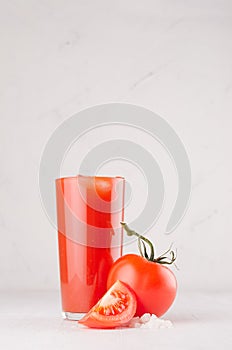 Healthy beverage - fresh vegetable tomato juice, straw, salt and red tomatoes on soft white wood background, copy space, vertical.