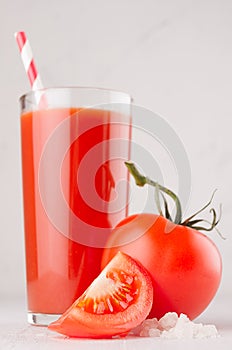 Healthy beverage - fresh vegetable tomato juice, straw, salt and red tomatoes on soft white wood background, macro, vertical.