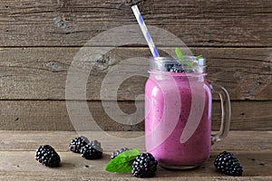 Blackberry smoothie in a mason jar with scattered berries over wood