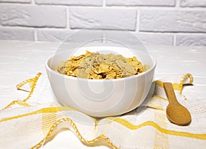 Healthy Bowl of Corn Flakes and Wooden Spoon on Yellow Napkin on White backround