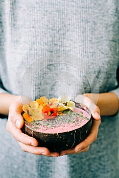 Healthy breackfast in bowl of coconut with nasturtium flowers in hands on white background