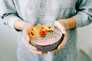 Healthy breackfast in bowl of coconut with nasturtium flowers in hands on white background