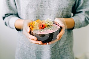 Healthy breackfast in bowl of coconut with nasturtium flowers in hands on white background