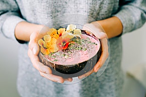 Healthy breackfast in bowl of coconut with nasturtium flowers in hands on white background