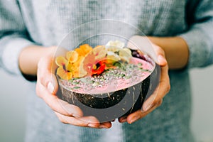 Healthy breackfast in bowl of coconut with nasturtium flowers in hands on white background