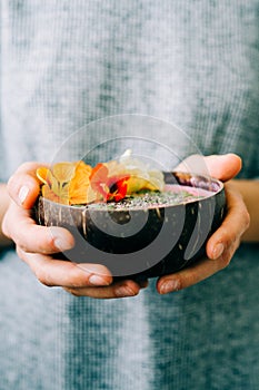 Healthy breackfast in bowl of coconut with nasturtium flowers in hands on white background