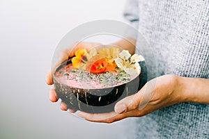 Healthy breackfast in bowl of coconut with nasturtium flowers in hands on white background