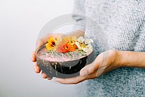 Healthy breackfast in bowl of coconut with nasturtium flowers in hands on white background