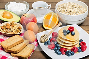 Healthy breakfast background with coffee  pancakes  fresh berries  eggs  avocado  greek yogurt  oats  rusks and orange