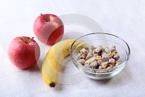 Healthy breakfast with banana, apple and Fresh granola, muesli in bowl on textile background. Top view.