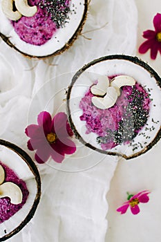 Healthy Breakfast berry smoothie with Chia seeds and cashew nuts in a natural coconut plate on a white table with pink flowers