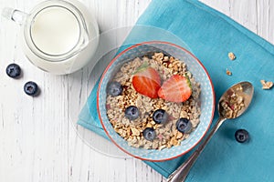 Healthy breakfast, bowl with granola muesli with strawberry and blueberry and milk jug, wooden background, top view