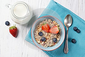 Healthy breakfast, bowl with granola muesli with strawberry and blueberry and milk jug, wooden background, top view