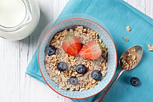 Healthy breakfast, bowl with granola muesli with strawberry and blueberry and milk jug, wooden background, top view