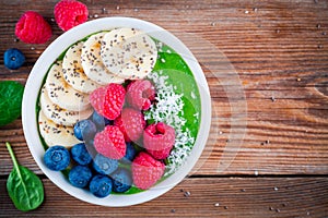 Healthy breakfast bowl: green spinach smoothie with banana, blueberries, raspberries, chia seeds and coconut