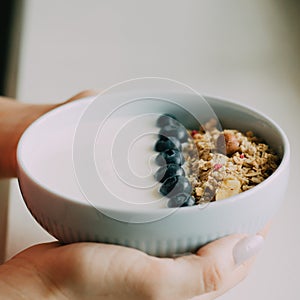 Healthy breakfast bowl with muesli and yogurt in woman hands on pink and marble background.