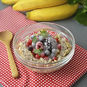 Healthy breakfast in a bowl with oatmeals, frozen berries, fresh strawberries, mint. Oat porridge with fruits. Square image