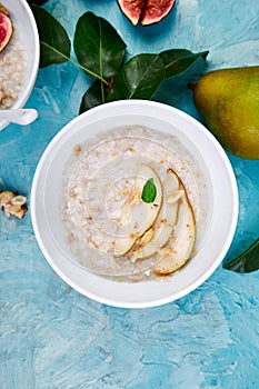 Healthy breakfast. A bowl of porridge with pears slices and walnuts on blue background.