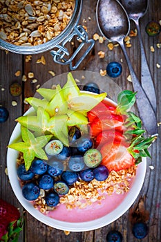 Healthy breakfast bowl: raspberry smoothies with granola, blueberries, strawberries and carambola