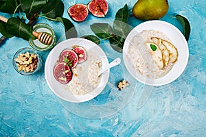 Healthy breakfast. A bowls of porridge with pears slices and walnuts and porridge with figs on blue background.