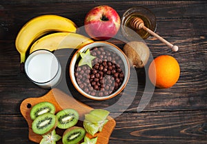 Healthy breakfast - cereal chocolate balls, milk and fruit on wood background