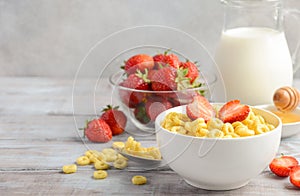 Healthy breakfast - cereal in a white bowl with strawberries, milk and honey