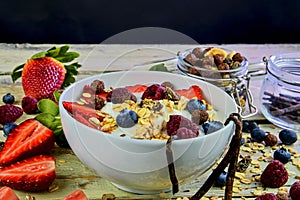 Healthy breakfast, cereal with yoghurt, strawberries, blueberries, raspberries and muesli on wooden rustic background
