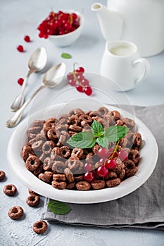 Healthy breakfast with chocolate corn rings, red currant berries, yogurt and tea on a gray concrete background. Selective focus.