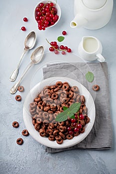 Healthy breakfast with chocolate corn rings, red currant berries, yogurt and tea on a gray concrete background. Selective focus.