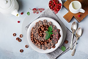 Healthy breakfast with chocolate corn rings, red currant berries, yogurt and tea on a gray concrete background. Selective focus.