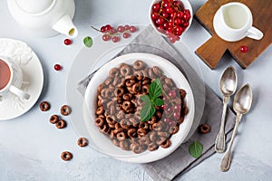 Healthy breakfast with chocolate corn rings, red currant berries, yogurt and tea on a gray concrete background. Selective focus.