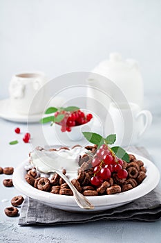 Healthy breakfast with chocolate corn rings, red currant berries, yogurt and tea on a gray concrete background. Selective focus.