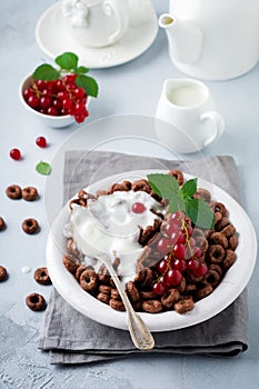 Healthy breakfast with chocolate corn rings, red currant berries, yogurt and tea on a gray concrete background. Selective focus.