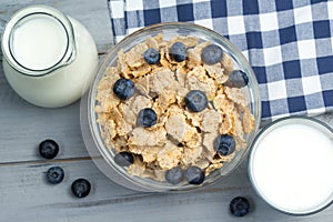 Healthy breakfast concept - bowl of cereals with fresh blueberries, glass and jug of milk